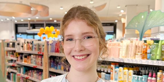 Drogistin in Ausbildung steht lächelnd vor Haarpflege-Regal im dm-Markt