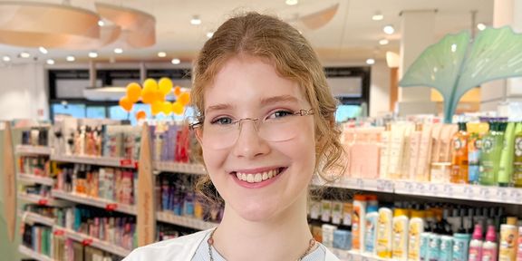 Drogistin in Ausbildung steht lächelnd vor Haarpflege-Regal im dm-Markt