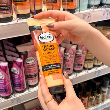 Angehende Drogistin hält ein Balea Locken Shampoo vor einem Regal im dm-Markt in der Hand