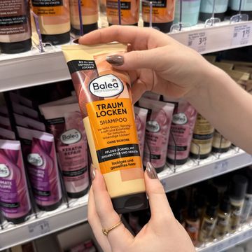 Angehende Drogistin hält ein Balea Locken Shampoo vor einem Regal im dm-Markt in der Hand