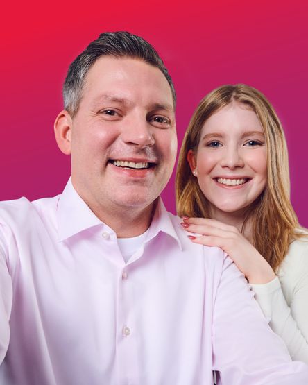 Ein Mann und eine Frau lächeln vor einem lebhaften rosa Farbverlaufshintergrund. Die Frau legt ihre Hand auf die Schulter des Mannes.