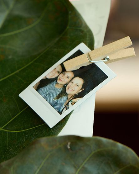 Polaroid mit drei Menschen. Das Bild ist mit einer Holzwäscheklammer an das Blatt einer Zimmerpflanze gepinnt.