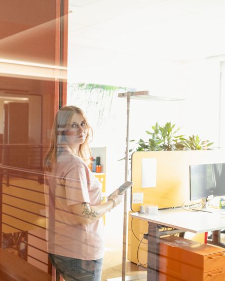junge Frau mit Smartphone steht an der Glaswand im Büro eines dm-Logistikzentrums
