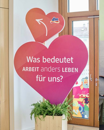 Figur aus zwei Herzen mit dm-Logo und Aufschrift "Was bedeutet Arbeit anders leben"