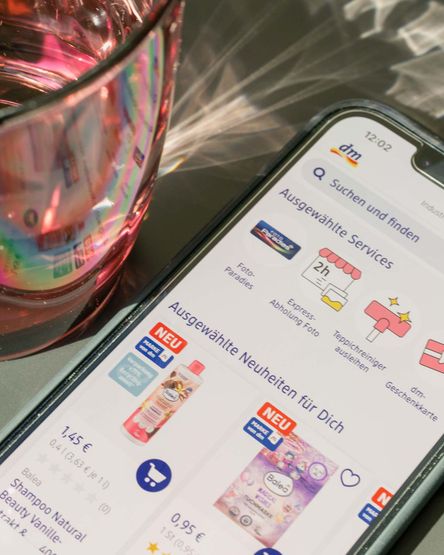 Smartphone mit offenem dm-Onlineshop neben Wasserglas