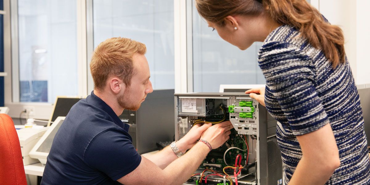 Angehender Fachinformatiker und Ausbilderin reparieren Rechner im Technikraum