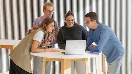 Vier dmTECH-Mitarbeitende im Austausch vor Laptop