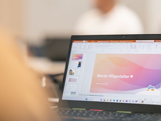 dm-Mitarbeitender vor Laptop mit offener PowerPoint-Präsentation