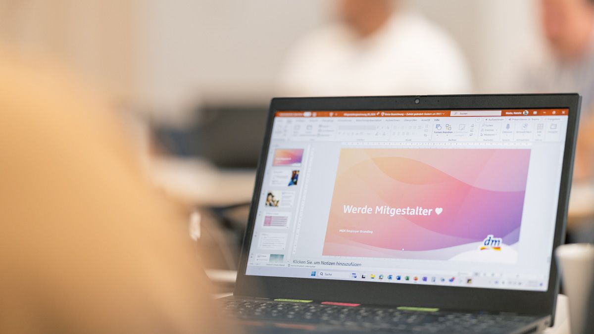 dm-Mitarbeitender vor Laptop mit offener PowerPoint-Präsentation