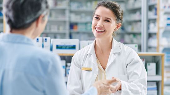 Lächelnde Apothekerin reicht einem Kunden an der Ladentheke ein Produkt