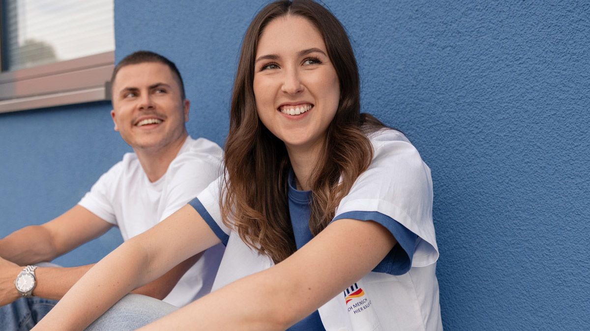Zwei fröhliche dm-Studierende vor blauer Wand eines dm-Markts