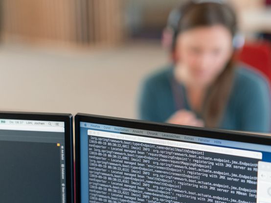 Rechner mit Code und dmTECH-Mitarbeitende im Hintergrund