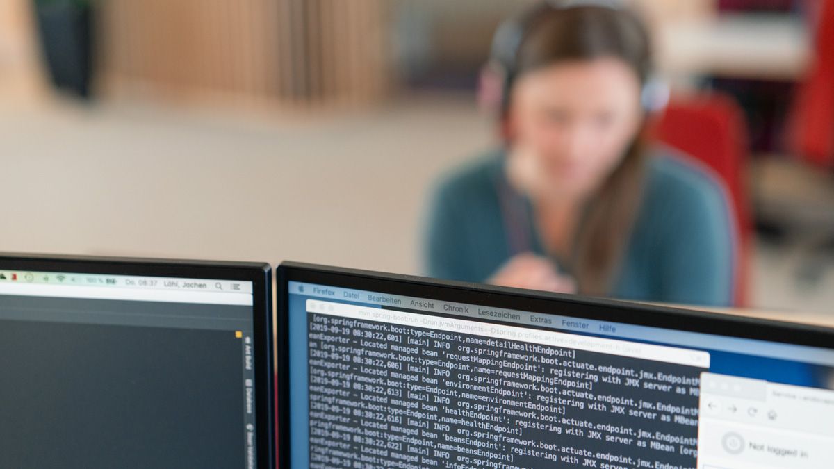 Rechner mit Code und dmTECH-Mitarbeitende im Hintergrund