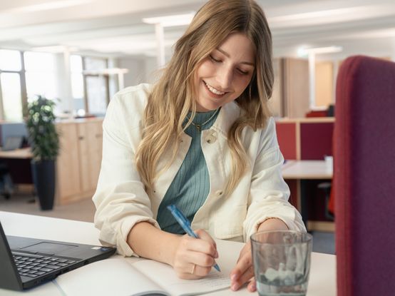 Studierende arbeitet am Laptop und macht Notizen im Heft im dm-Unternehmenssitz