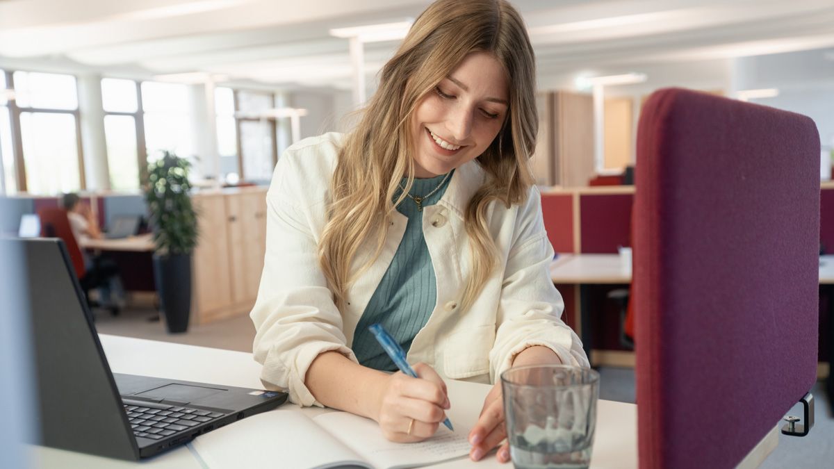 Studierende arbeitet am Laptop und macht Notizen im Heft im dm-Unternehmenssitz