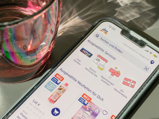Smartphone mit offenem dm-Shop neben rotem Wasserglas