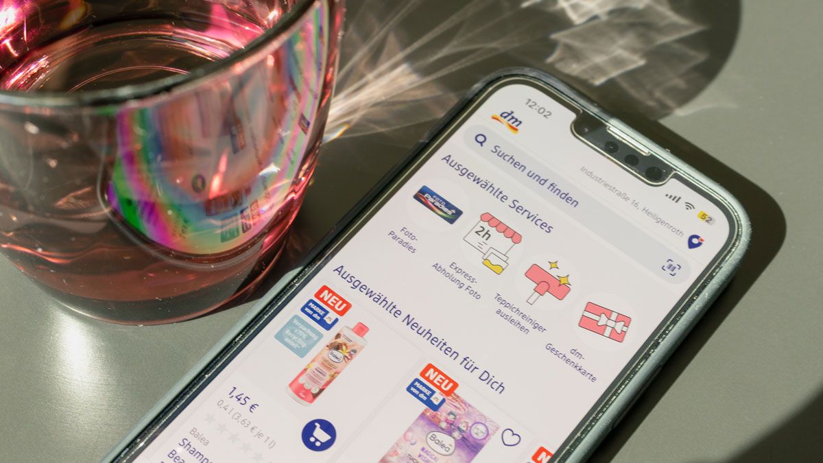 Smartphone mit offenem dm-Shop neben rotem Wasserglas