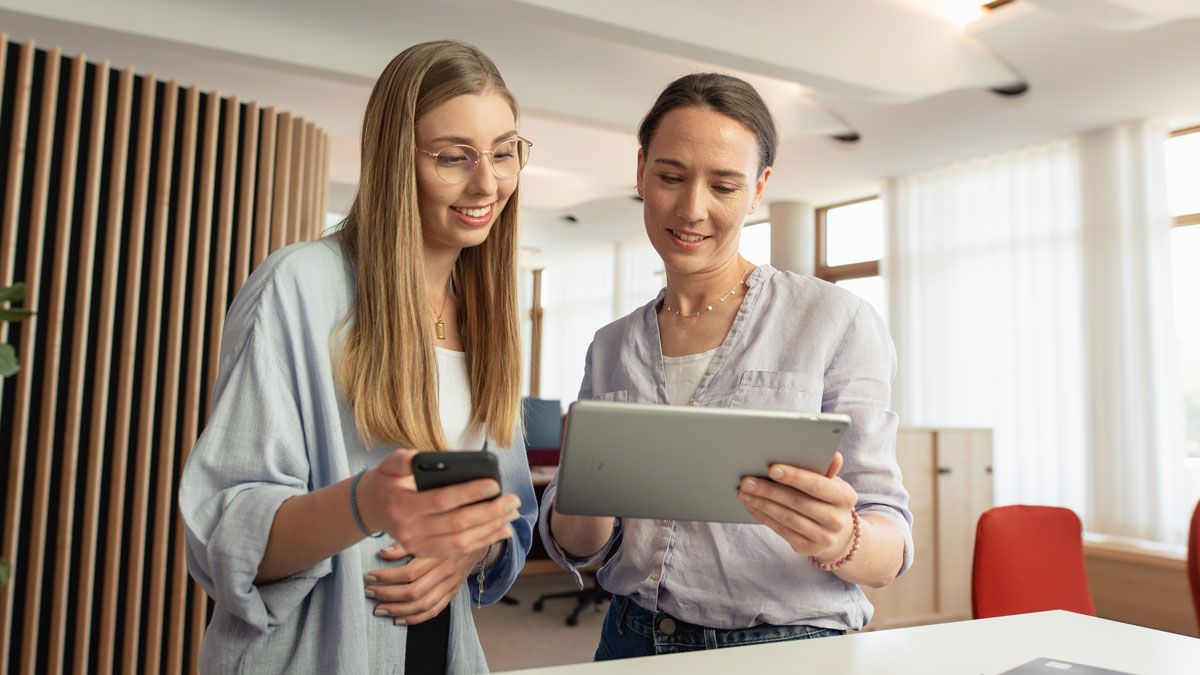 Angehende Kauffrau für Marketingkommunikation mit Ausbilderin gleichen Infos auf Smartphone und Tablet ab