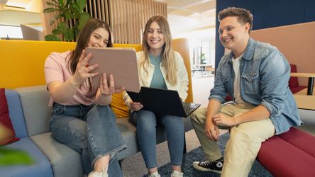 Drei junge Menschen in Ausbildung im Gespräch vor Laptop und Tablet