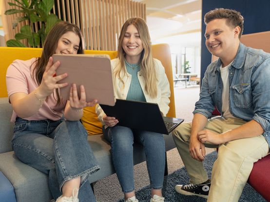 Drei junge Menschen in Ausbildung im Gespräch vor Laptop und Tablet