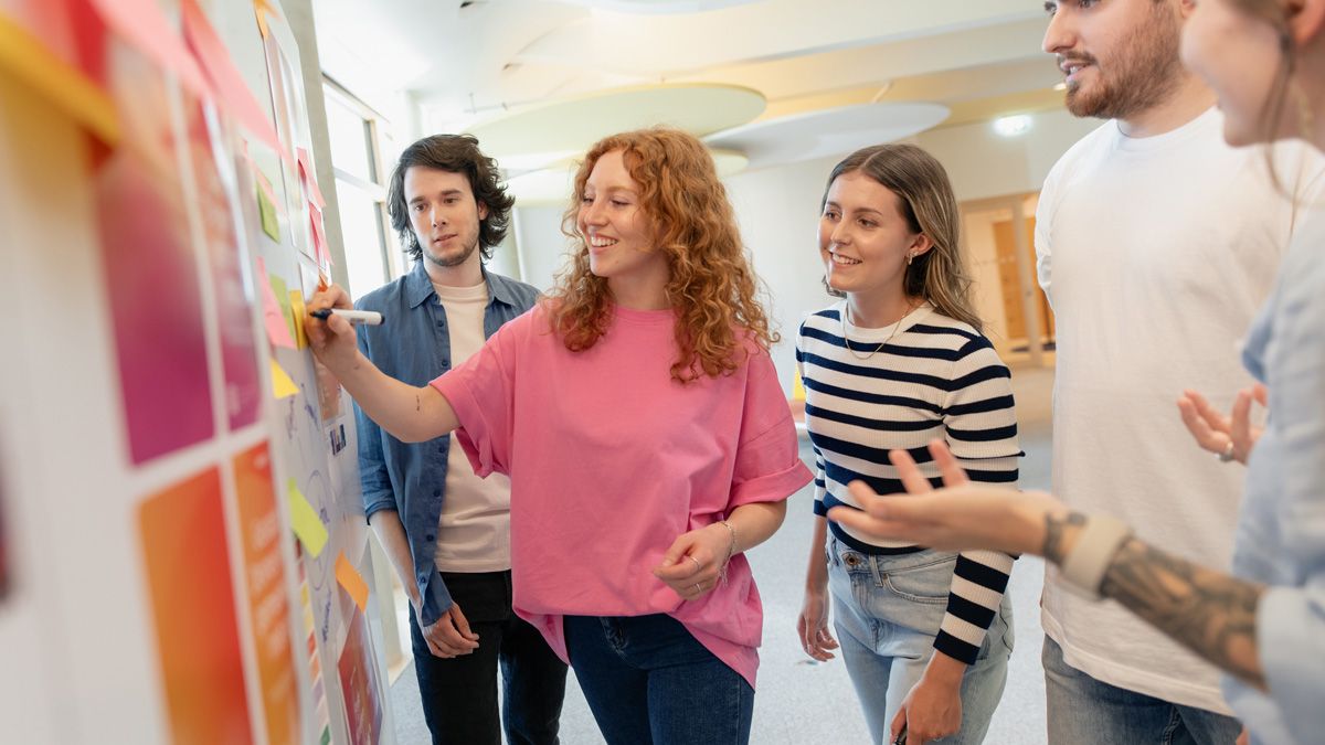 Drei dm-Studierende brainstormen mit Ausbildern am Whiteboard