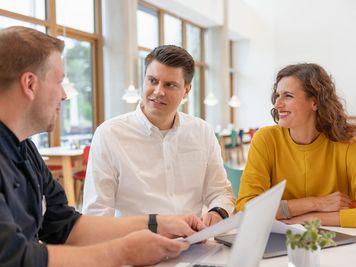 zwei Männer und eine Frau unterhalten sich am Tisch sitzend