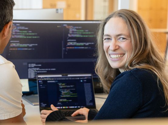 lächelnde Softwareentwicklerin vor mehreren Monitoren