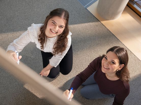Zwei dunkelhaarige Frauen schreiben auf ein Whiteboard