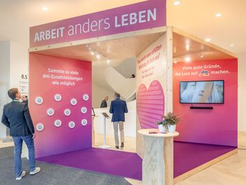 Ausstellungsstand in rosa und Holzdesign mit interaktiven Displays und Text über das Arbeiten bei dm-drogerie markt. Die Menschen beschäftigen sich mit den Displays.