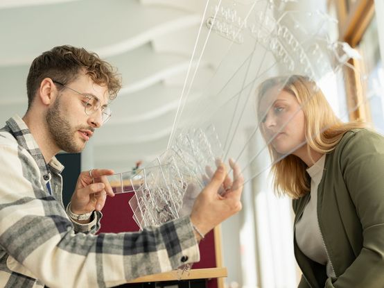 Zwei Personen, die transparente Warentrenner untersuchen. Der Mann weist auf Details hin, während die Frau in einem gut beleuchteten Raum genau hinschaut.
