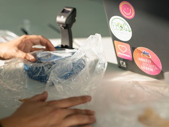 Hände messen Foliendichte auf einem Tisch, daneben steht ein Laptop mit bunten Aufklebern.