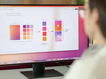 Person, die einen Computerbildschirm betrachtet, der ein Farbschema und Designelemente mit Farbverläufen und Farbfeldern anzeigt.