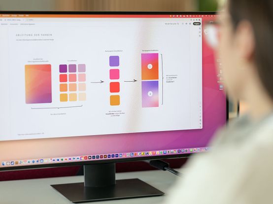 Person, die einen Computerbildschirm betrachtet, der ein Farbschema und Designelemente mit Farbverläufen und Farbfeldern anzeigt.