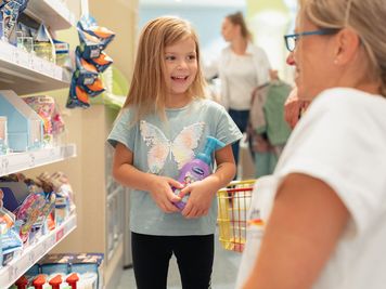 blondes Mädchen mit Kinderdusche spricht mit dm-Verkäuferin