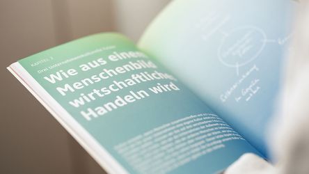 Aufgeschlagenes Buch zum Thema "wie aus einem Menschenbild wirtschaftliches Handeln wird"