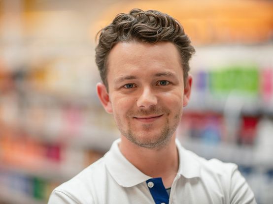 dm-Verkäufer vor einem Regal schaut freundlich in die Kamera