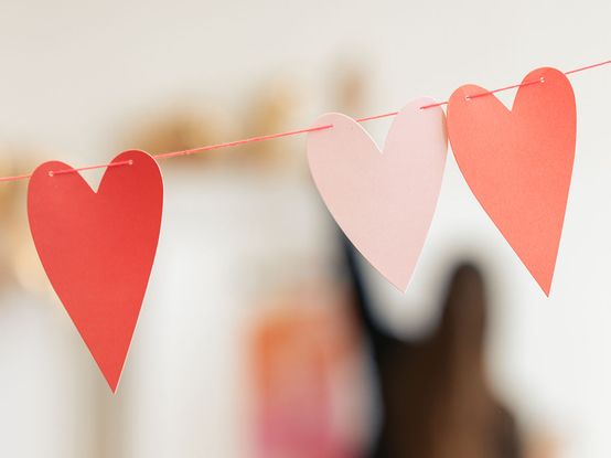 Drei Papierherzen, zwei rote und ein rosa, hängen an einer Schnur vor einem verschwommenen Hintergrund.