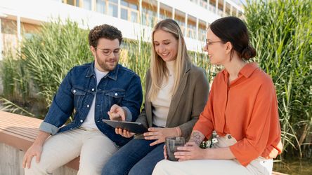 dm-Studierende mit Tablet und Ausbilderin im Gespräch vor dm-Unternehmenssitz