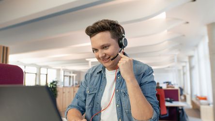 Junger Mann mit Headset telefoniert über Laptop