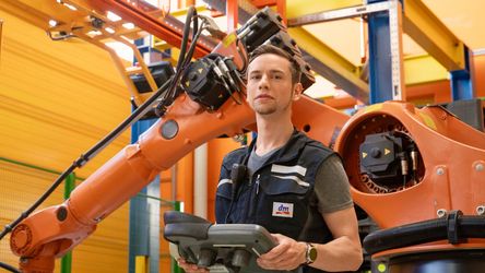 Angehender Mechatroniker mit Bedienpanel prüft Funktionalität von Roboterarm