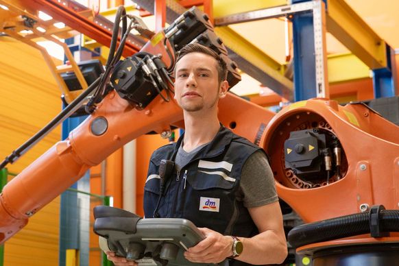 Angehender Mechatroniker mit Bedienpanel prüft Funktionalität von Roboterarm